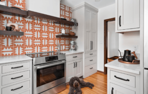 A dog sitting in a recently remodeled kitchen with stainless steel appliances and open shelving.