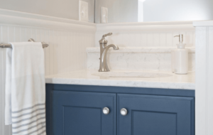 A small bathroom remodel with a blue vanity, white countertop and gray walls.
